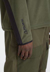 Langärmliges trui in olijfgroen fleece met zwarte accenten, voorzien van het "Polartec"-logo op de mouw. Zachte textuur, casual ontwerp.