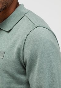 Hellgrünes Poloshirt aus weichem Stoff. Verfügt über einen klassischen Kragen, kurze Ärmel und ein dezentes Logo auf der Brust.
