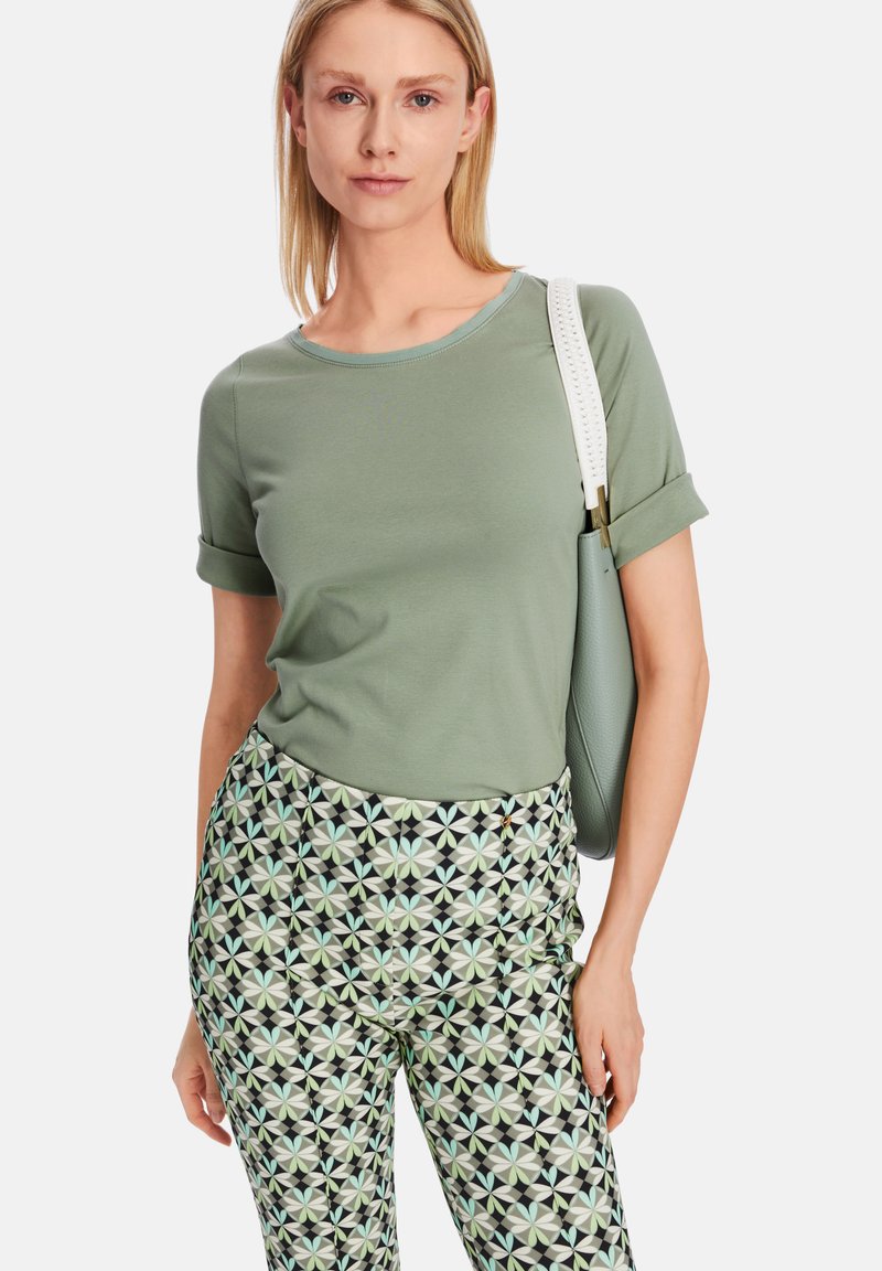 Helles grünes T-Shirt mit kurzen Ärmeln und rundem Ausschnitt, kombiniert mit gemusterten schwarzen und pastellfarbenen Hosen mit geometrischen Designs.