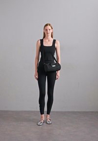 Top senza maniche nero e leggings, abbinati a una piccola borsa nera. Scarpe argentate eleganti riflettono la luce in modo sottile su uno sfondo neutro.