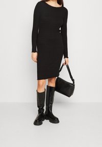 Vestito nero a maniche lunghe con un design aderente e orlo grezzo. Abbinato a stivali neri al ginocchio e una borsa nera con texture.