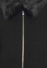 Giacca nera con colletto in pelliccia sintetica, chiusura frontale con cerniera, tessuto liscio e design minimalista. Nessun motivo o accento visibile.