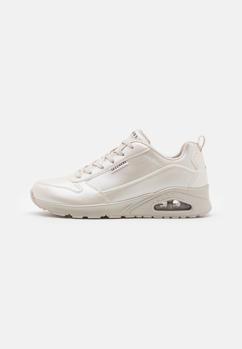 Baskets beige Skechers avec lacets à l'avant, semelle à coussin d'air visible et étiquette de marque sur le côté, vues de l'extérieur sur fond blanc.