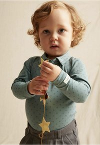 Vaaleansininen pitkähihaiseksi paita, jossa on hienovarainen kuvio, yhdistettynä harmaakuosisiiin housuihin. Lapsi pitää kädessään kultaisia tähtiä.