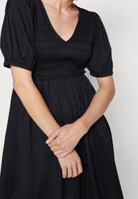 Svart klänning med puffärmar och djup V-ringning. Bygeln har samlat tyg, medan kjolen flödar löst till mittkalv.