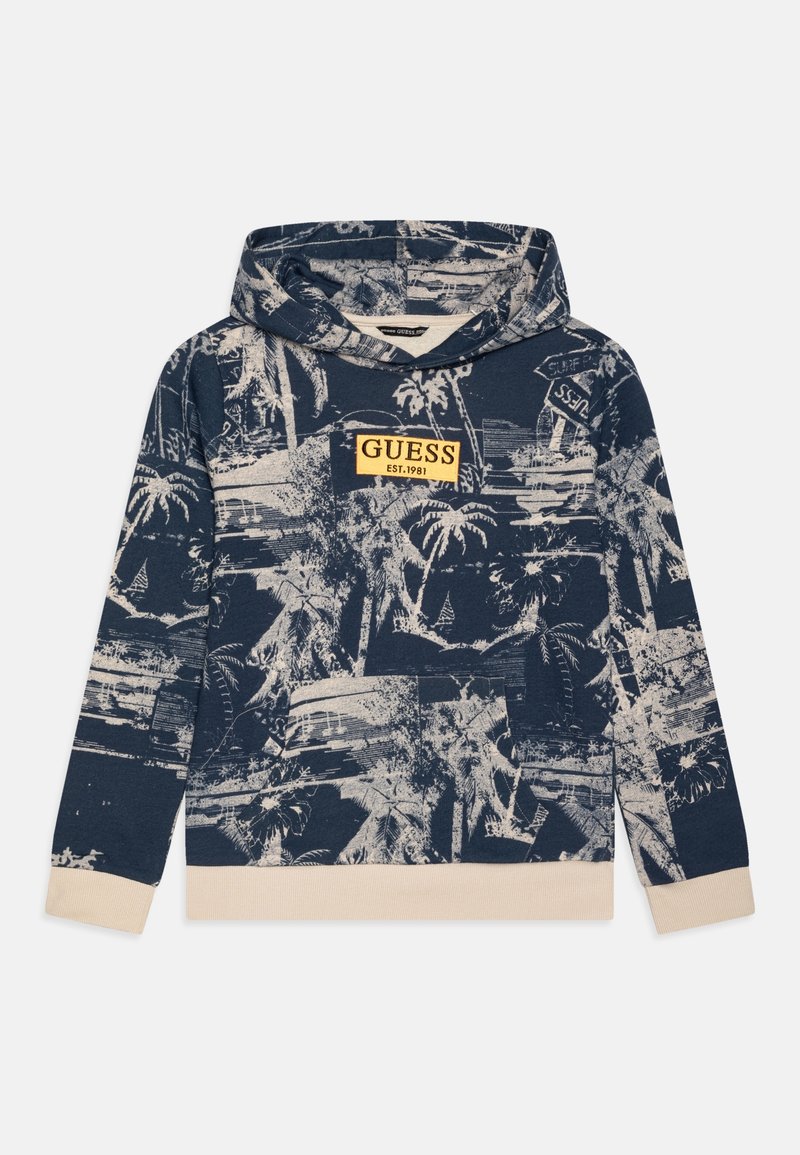 Sweat à capuche bleu marine avec poignets et ourlet beige, arborant un imprimé complet de palmiers tropicaux et un patch logo jaune "GUESS EST. 1981" sur la poitrine.