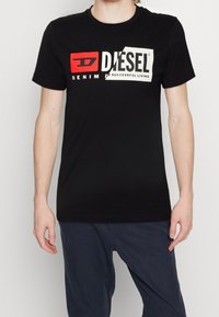 Czarna bawełniana koszulka z krótkim rękawem, z odważnym, graficznym logo w czerwonym i białym kolorze. Okrągły dekolt. Gładka tekstura.