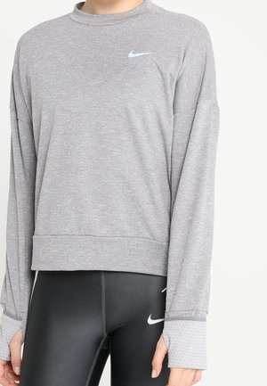 Sweat-shirt Nike gris à manches longues avec un col ras du cou, arborant un petit logo sur la poitrine et des poignets texturés, associé à des leggings noirs.