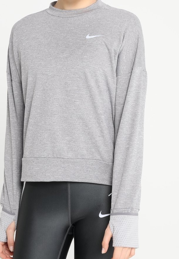 Felpa Nike grigia a maniche lunghe con collo a giro, caratterizzata da un piccolo logo sul petto e polsini texturizzati, abbinata a leggings neri.