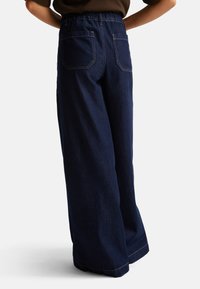 Široké tmavé džíny s nařaseným elastickým pasem, které mají dvě zadní kapsy a kontrastní švy.