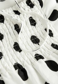 Tissu blanc à pois noirs avec une texture smockée et un cordon blanc. Vue en gros plan des détails du tissu.