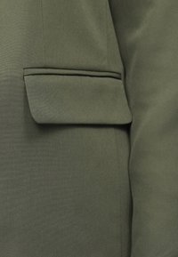 Olivovo zelený blazer s náprsní kapsou s preklápacím klapkou, hladkou textúrou látky a strihom na mieru.