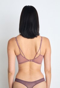 Bralette mauve avec des bretelles réglables et une fermeture à clip. Texture de tissu lisse avec un design minimaliste. String assorti avec un motif visible.