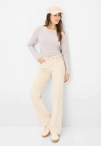 Gestreifte Langarmbluse in Lavendel und Weiß, beigefarbene hochgeschnittene Hose mit einem Gürtel und helle Sneakers mit einer Gummisohle.