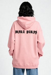 Felpa con cappuccio rosa in cotone, caratterizzata da una vestibilità rilassata, polsini a coste e la scritta "MIRA PARIS" stampata in nero con font gotico sul retro.