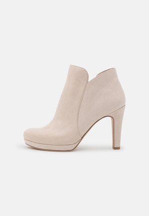 Bottine en daim beige avec talon haut, bout arrondi et légère semelle compensée, montrée de profil droit sur un fond uni.