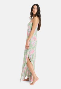 Vestido maxi en verde claro con estampado floral en rosa, con tirantes finos y una abertura lateral para facilitar el movimiento. Fabricado en tela ligera.
