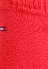 Calcetines de algodón rojos con una textura acanalada y un pequeño logo con acentos en azul, blanco y negro en el costado.