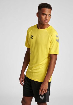 Geel sportshirt met korte mouwen en een gestructureerde afwerking, voorzien van een zwart logo en grijze chevronaccenten op de schouder, gecombineerd met zwarte shorts.
