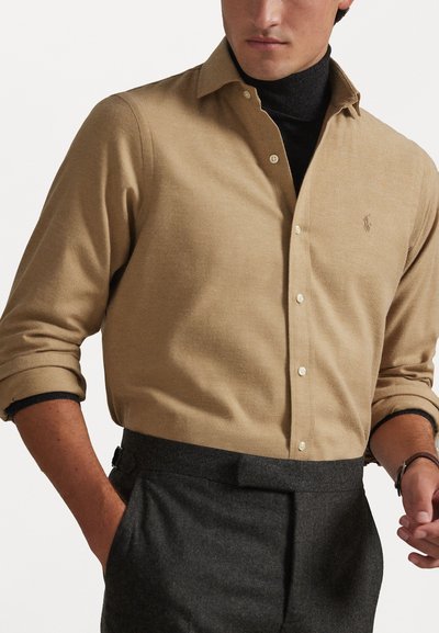 Camicia button-up beige realizzata in tessuto morbido con una sottile trama, dotata di un colletto classico e di un piccolo logo ricamato sul petto.