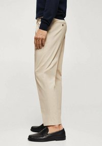 Pantaloni beige in cotone, con taglio dritto, tasche laterali e dettaglio con bottone sul retro, abbinati a mocassini neri.