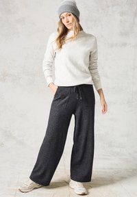 Suéter de punto gris claro con cuello redondo, combinado con pantalones de chándal gris oscuro de pierna ancha que tienen dos bolsillos delanteros y cinturilla con cordón.