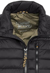 Sort pufferjakke med lynlås, der har en grøn foring og "Camel Active" logo. Stoffet ser glat ud med en quiltet tekstur.