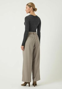 Grijze top met lange mouwen, gecombineerd met beige wijd uitlopende broeken. De outfit heeft een strakke pasvorm, een zachte textuur en subtiele ontwerpdetails.