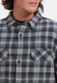 Czarna i biała koszula flanelowa w kratę z kołnierzykiem na guziki, dwoma kieszeniami na piersi i teksturowaną tkaniną. Charakteryzuje się widocznymi guzikami i wzorem w kratę.