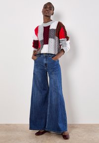 Sweter dziany z wielokolorowymi wzorami w czerwonym, szarym, brązowym i białym kolorze, zestawiony z szerokimi dżinsami w niebieskim kolorze. Błyszczące bordowe baleriny.