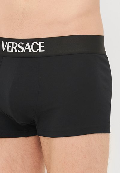 Svarte boksershorts med tett passform, laget av et glatt stoff og med en elastisk midjebånd merket med "VERSACE" i hvitt.