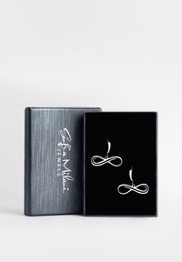 Silver infinity-formade  örhängen som visas i en svart sammetstoppad låda, med en texturerad metallisk grå yta som har en signaturlogotyp.