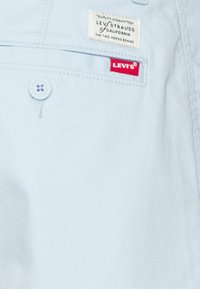 Gros plan sur une poche de vêtement Levi's bleu clair montrant le bouton, l'étiquette cousue et l'étiquette rouge de la marque Levi's.