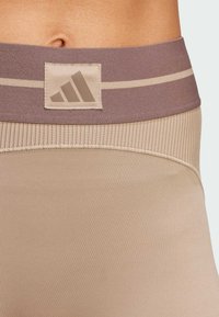 Beige atletiske leggings med en bred, brun talje, der har et prægget logo og vandret striber. Glat, strækbart stof.