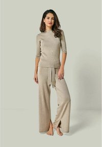 Strick-Zweiteiler in hellbeige, bestehend aus einem figurbetonten Kurzarmoberteil und weit geschnittenen Hosen mit einem Bindeband an der Taille und seitlichen Schlitzen.