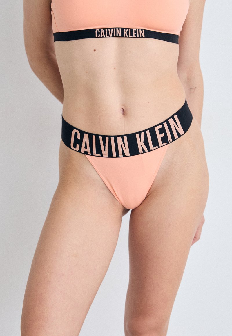 Calvin Klein bikini set in perzik met een zwarte tailleband waarop de merknaam in roze letters staat. Glad materiaal met een minimalistisch ontwerp.