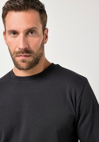 Sort crewneck t-shirt lavet af glat stof, med lange ærmer og en afslappet pasform. Detaljer inkluderer en subtil tekstur og ingen synlige grafik.