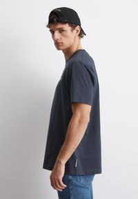 Mørkeblå bomull T-skjorte med korte ermer, rund hals og liten logo på brystet; brukt med slitte lyseblå jeans.