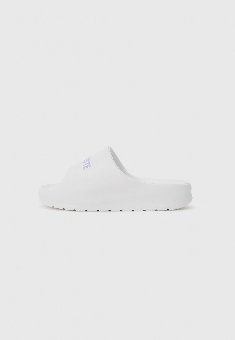 Sandale blanche à semelle lisse, design ouvert à l'avant et un léger plateau. Présente un logo violet discret sur le dessus.