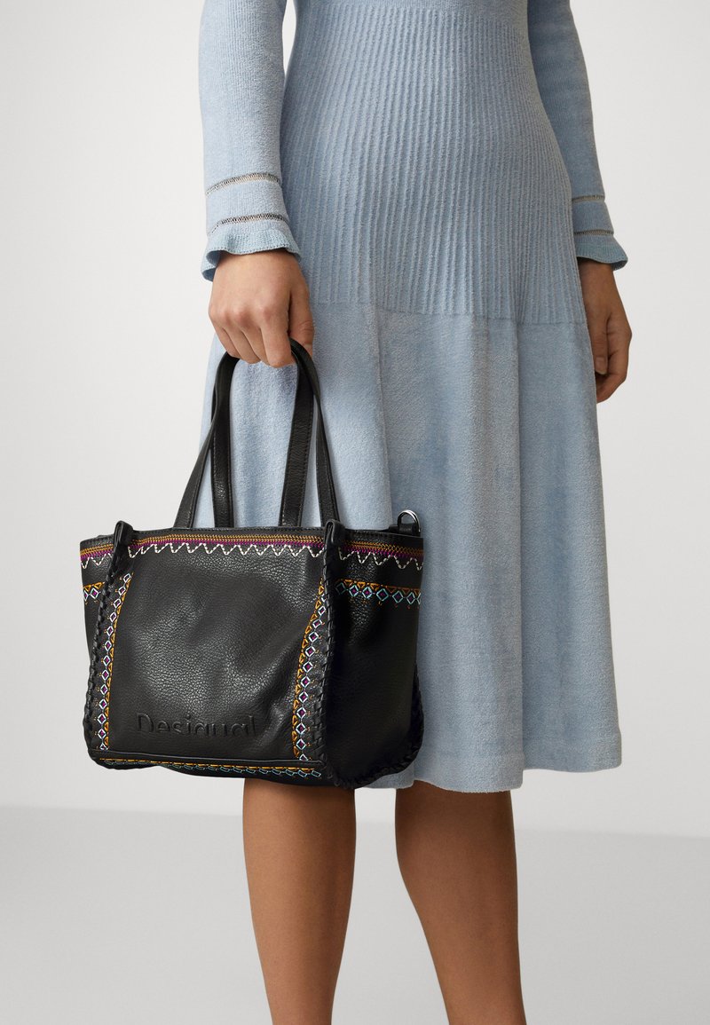 Schwarze Lederhandtasche mit bunten Stickakzenten, strukturierter Oberfläche und zwei Griffen. Logo auf der Vorderseite geprägt.