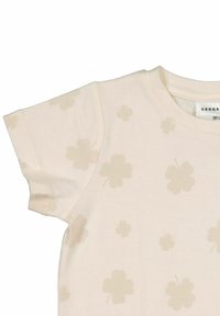 Ljust beige kortärmad t-shirt med ett blommönster av svaga klöver, med rund halsringning och mjuk bomullstextur.