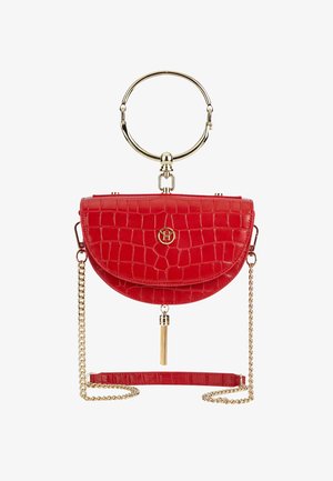 Sac à main rouge demi-lune avec texture crocodile, poignée circulaire dorée, bandoulière chaîne dorée et détail pompon doré en bas au centre.