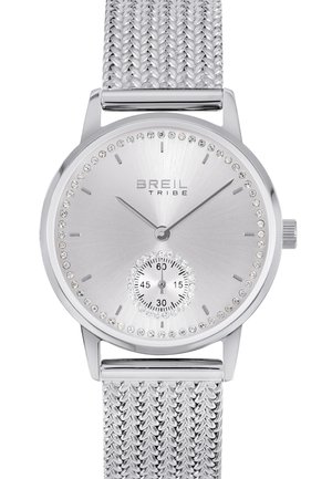 Sølvur med et mesh-bånd i rustfrit stål, rund urskive, krystalakcenter omkring urskiven og en mindre sekundviser.