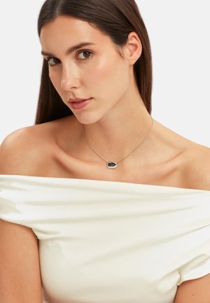 Sølv kæde med en poleret, oval sort vedhæng. Glat tekstur med en blank finish, vist på en model med en off-shoulder top.