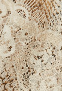 Tissu en dentelle crème présentant des motifs floraux délicats, des franges délicates le long des bords et un tissage doux et texturé.