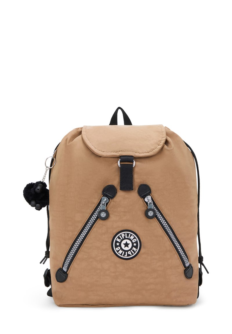 Mochila de nylon color beige con una solapa redondeada, cremalleras negras, parche de logo circular y un llavero de pompones. Correas ajustables y asa en la parte superior.