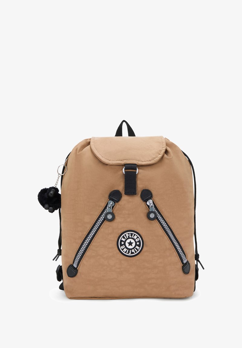 Mochila de nylon color beige con una solapa redondeada, cremalleras negras, parche de logo circular y un llavero de pompones. Correas ajustables y asa en la parte superior.
