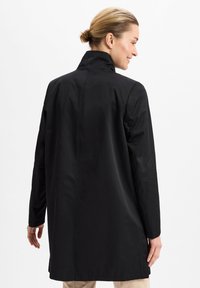Schwarzer, langer Mantel aus glattem Stoff, mit hohem Kragen und geradem Schnitt. Der Rücken hat minimale Nähte und ein sauberes Design.