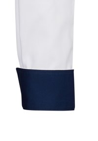 Camicia bianca con polsino blu navy. Il polsino presenta una texture liscia e un colore uniforme, in contrasto con il tessuto bianco sopra.