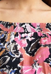 Tissu à motif floral avec des fleurs roses, orange et bleues sur un fond noir, doté d'un col froncé et élastique pour plus de souplesse.